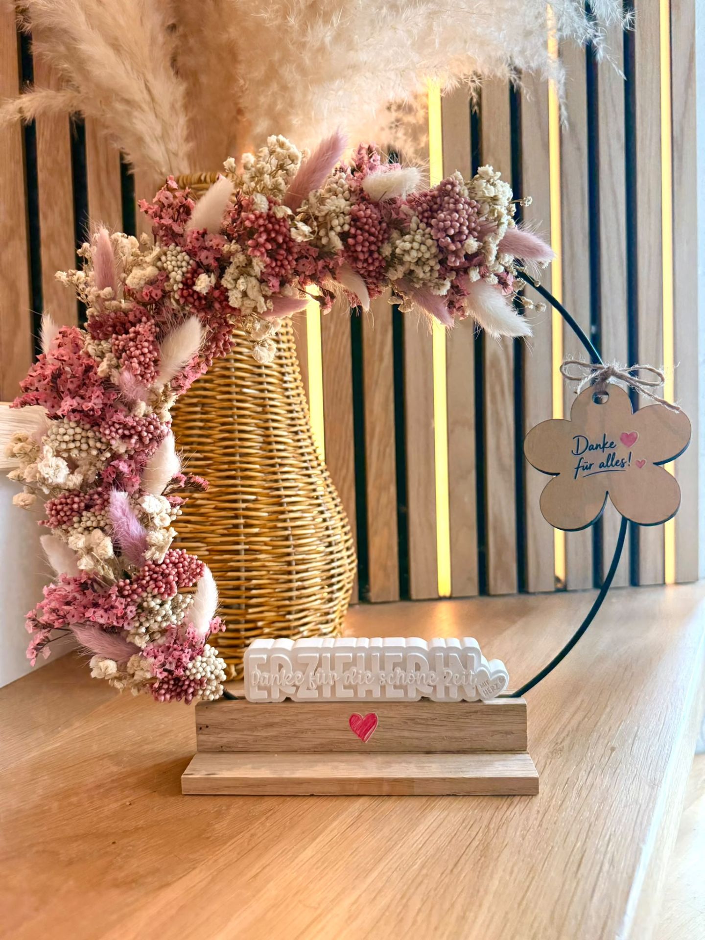 Abschiedsgeschenk aus rosa Trockenblumen mit einem beschrifteten Holzanhänger.