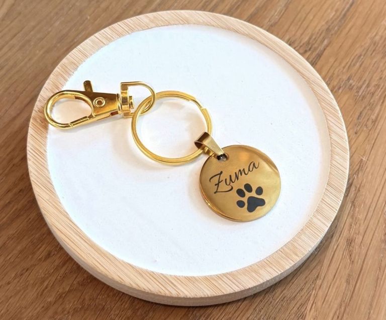 Goldfarbene Hundemarke mit Pfotenmotiv und Gravur auf einem Holztablett.