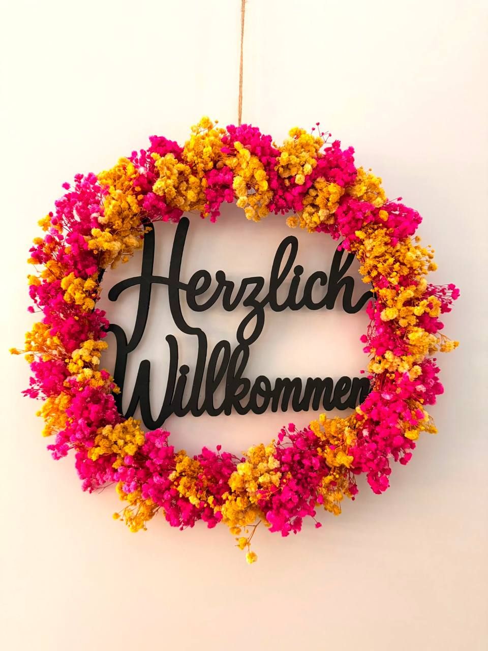 Runder Türkranz aus pinken und gelben Trockenblumen mit einem Schriftzug aus Holz.