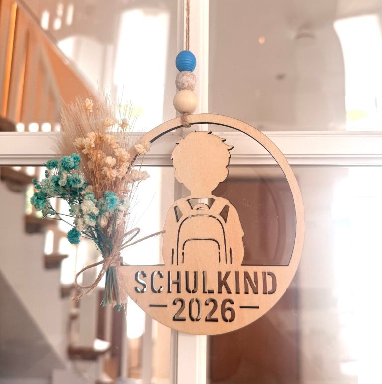 Runder Holzanhänger mit der Silhouette eines Schulkindes und Trockenblumen.