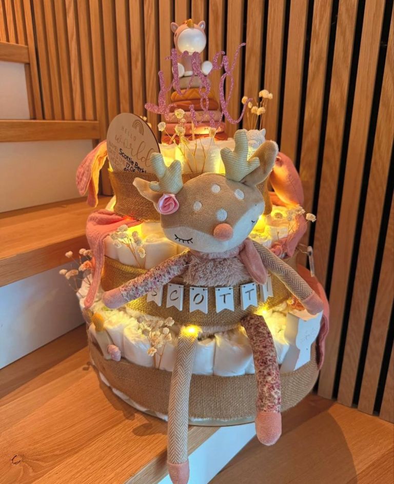 Mehrstöckige Windeltorte mit Schleifen, Lichterkette und einem Kuscheltier auf der Spitze.